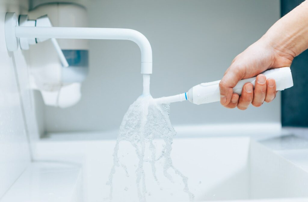 A close-up hand holding a toothbrush under flowing water from the faucet