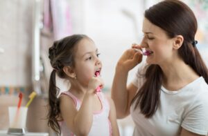 A woman brushing her teeth with her daughter, showing her how to brush teeth properly