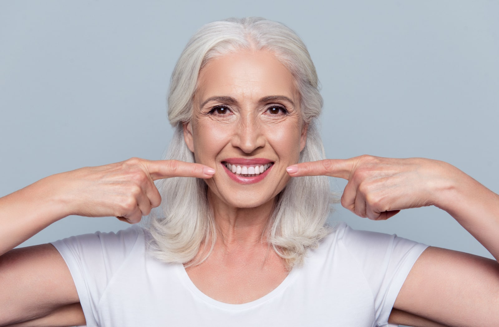 A woman with dental implants points to her new smile