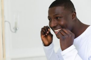 A young person in a white shirt flossing his teeth.