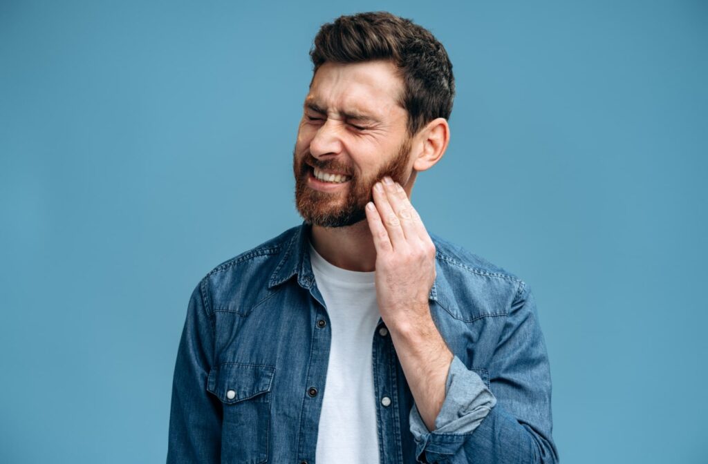 A man holds the side of his jaw because of pain, most likely due to a cavity.