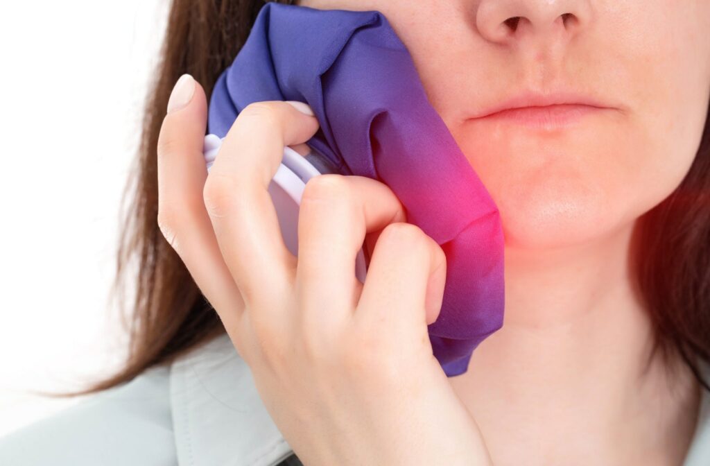 A woman is applying a cold compress to her cheek to ease jaw discomfort caused by TMJ