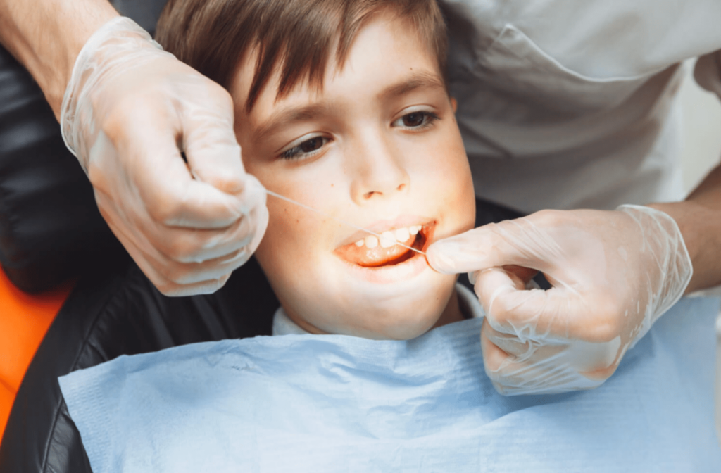 A close-up of a young boy comfortably seated in a dental chair, with the dentist meticulously flossing his teeth.