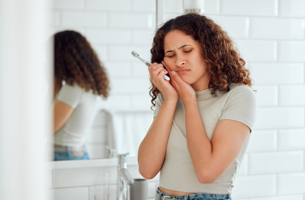 a woman is holding her mouth as she feels discomfort brushing her teeth from a cavity.