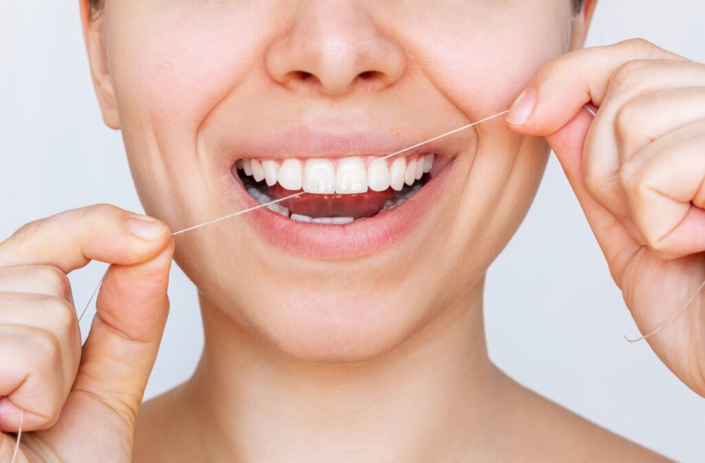 A young woman smiling while flossing to prevent gingivitis.