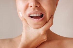 A close-up image of a young woman holding her jaw in discomfort due to gingivitis.