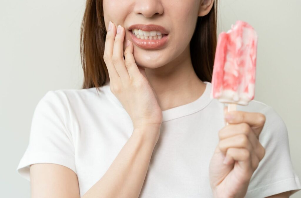 The bottom half of a woman's face is shown looking uncomfortable from tooth sensitivity after biting into a cold popsicle