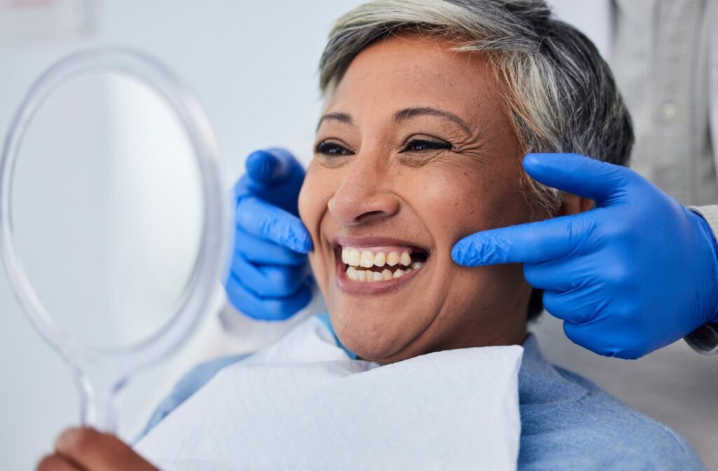 A patient holds up a mirror while a dentist points at their teeth during a dental exam.