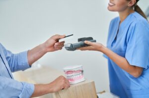 A dental hygienist smiles while helping a patient pay their co-payment for dental services covered by the CDCP.