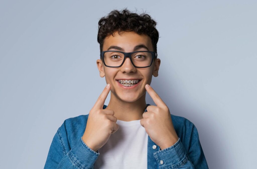 A teenager with braces smiling and pointing towards their mouth.