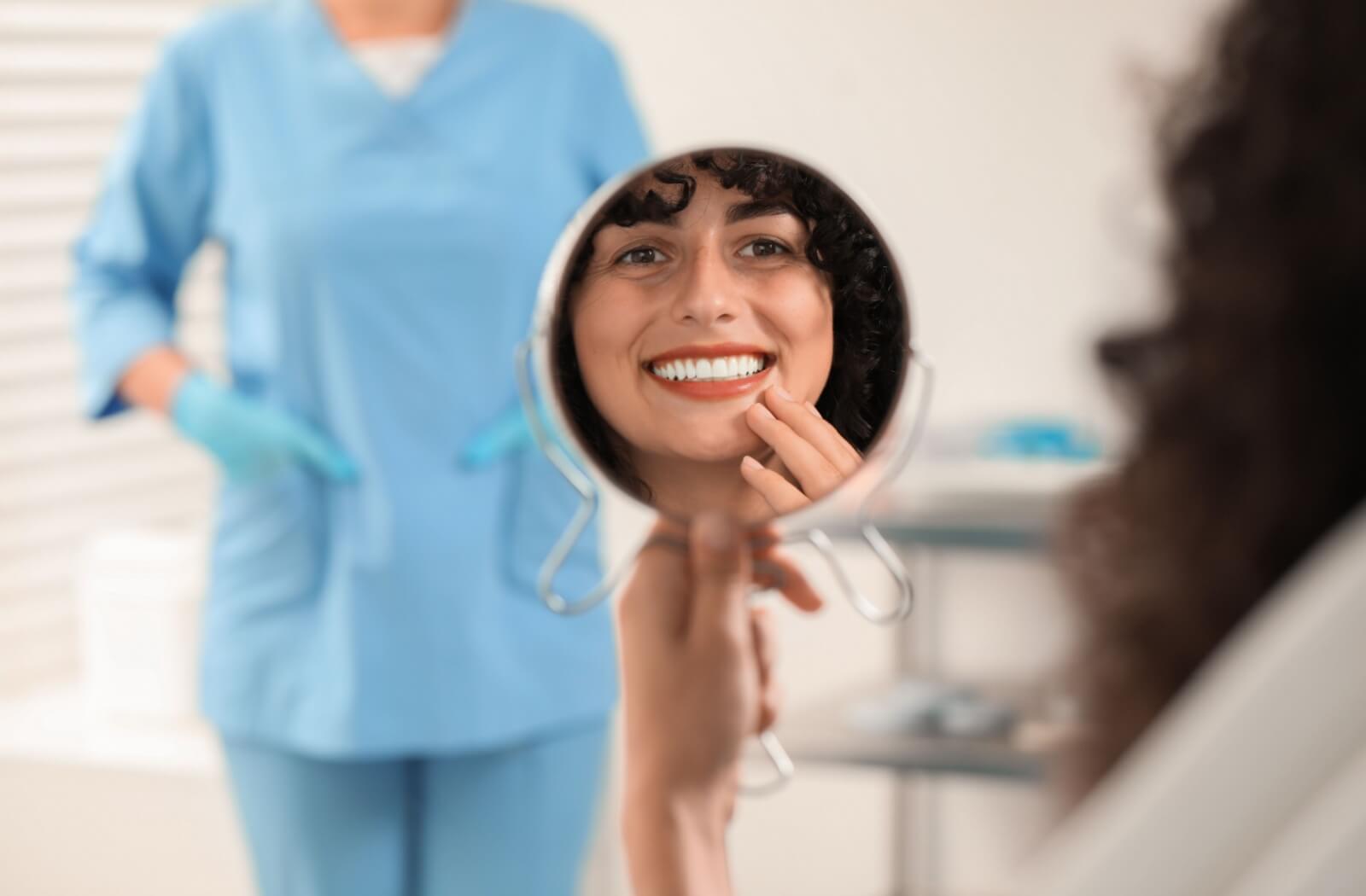 Patient smiling after veneers while looking at teeth in mirror at dental clinic.
