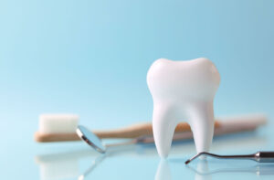 Model of a tooth with dental tools and a toothbrush on a light blue background.