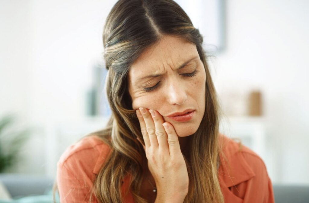 Woman holding her cheek in pain, showing discomfort from a toothache or dental problem.