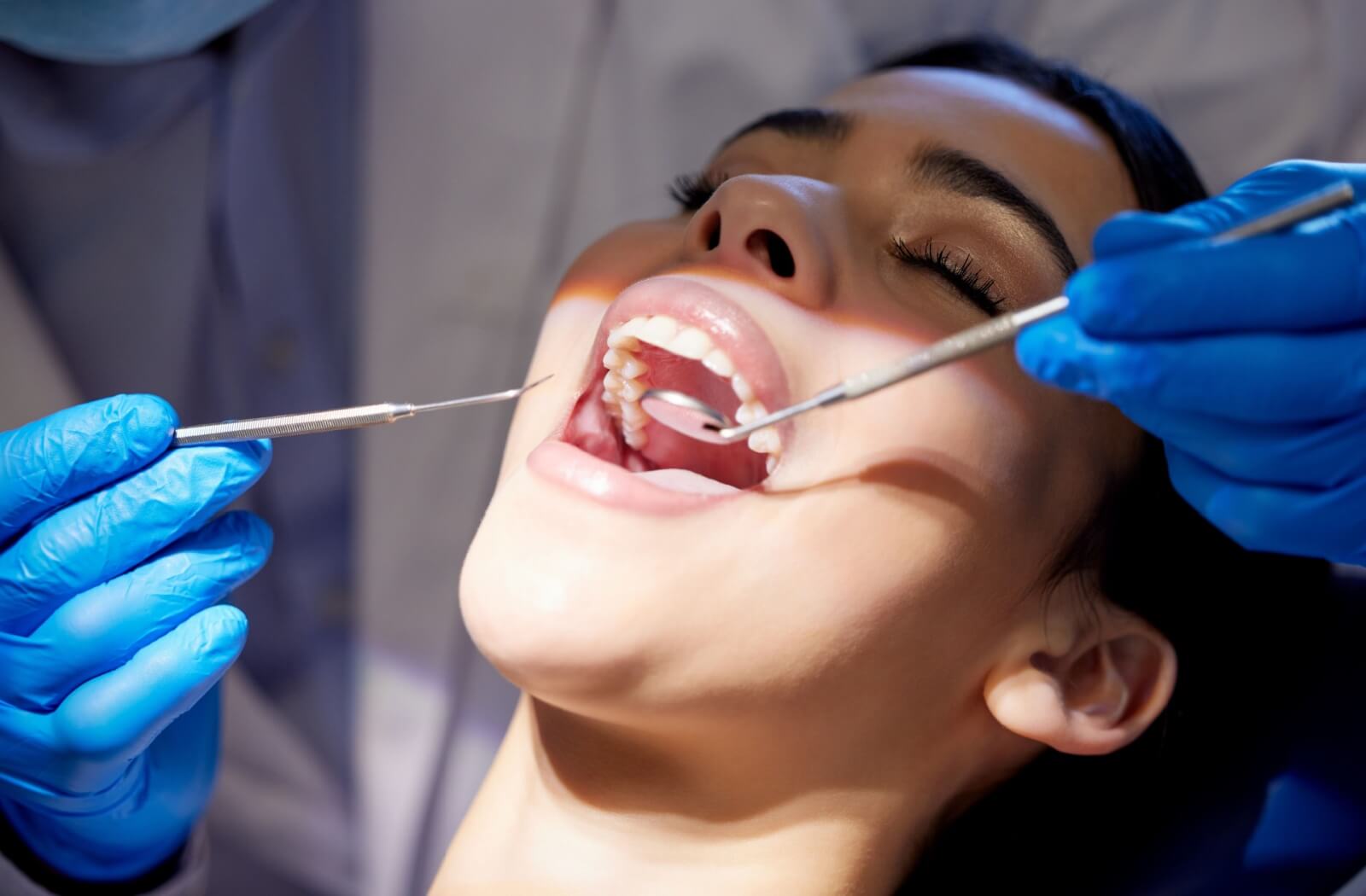 Dentist performing a routine dental exam using dental tools to examine a patient’s teeth.