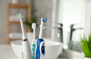 Three toothbrushes, including two electric and one manual, standing in a cup beside a bathroom sink