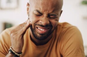 A man wincing and holding his jaw in pain, representing the discomfort and sensitivity often associated with advanced gum disease or periodontal infection.