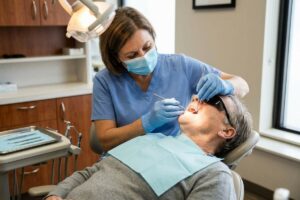 Dentist examines an adult's teeth with dental tools as the patient reclines in a dental chair.